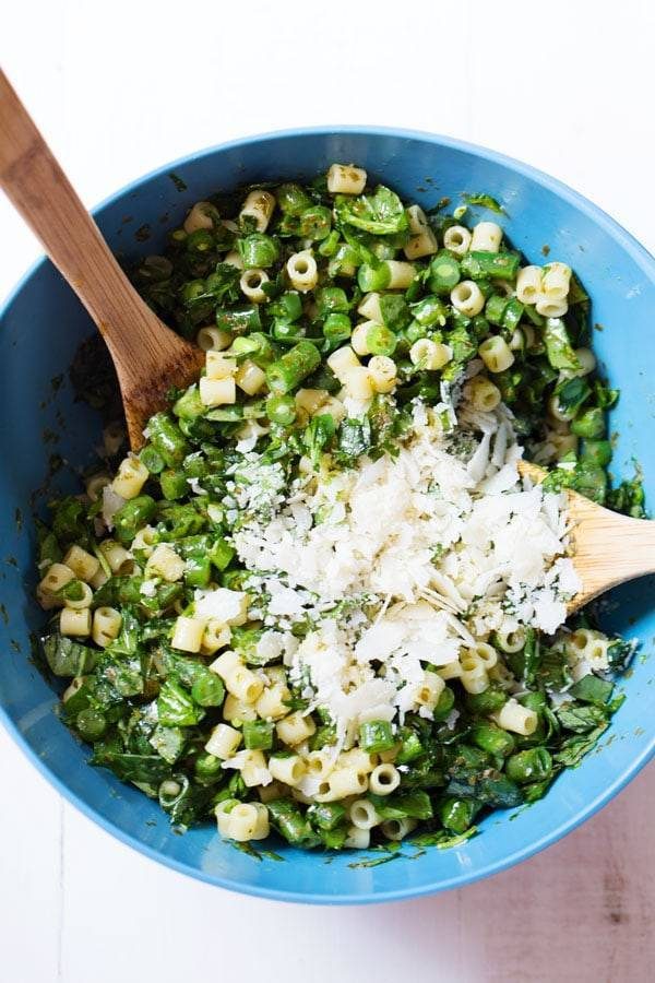 Pasta salad in a mixing bowl with wooden spoons.